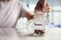 Foto: Person wirft Münzen in Glas mit Aufschrift Pension